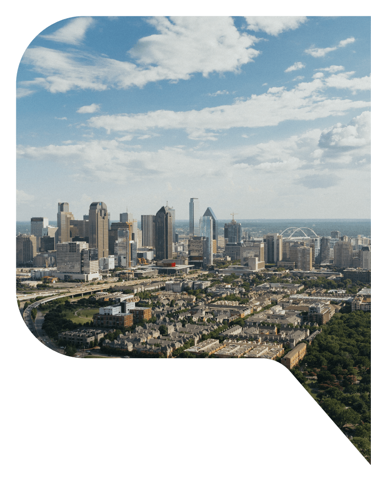 Aerial view of Dallas, Texas with a raised highway leading into the city from the left and a double-arched bridge in the background.